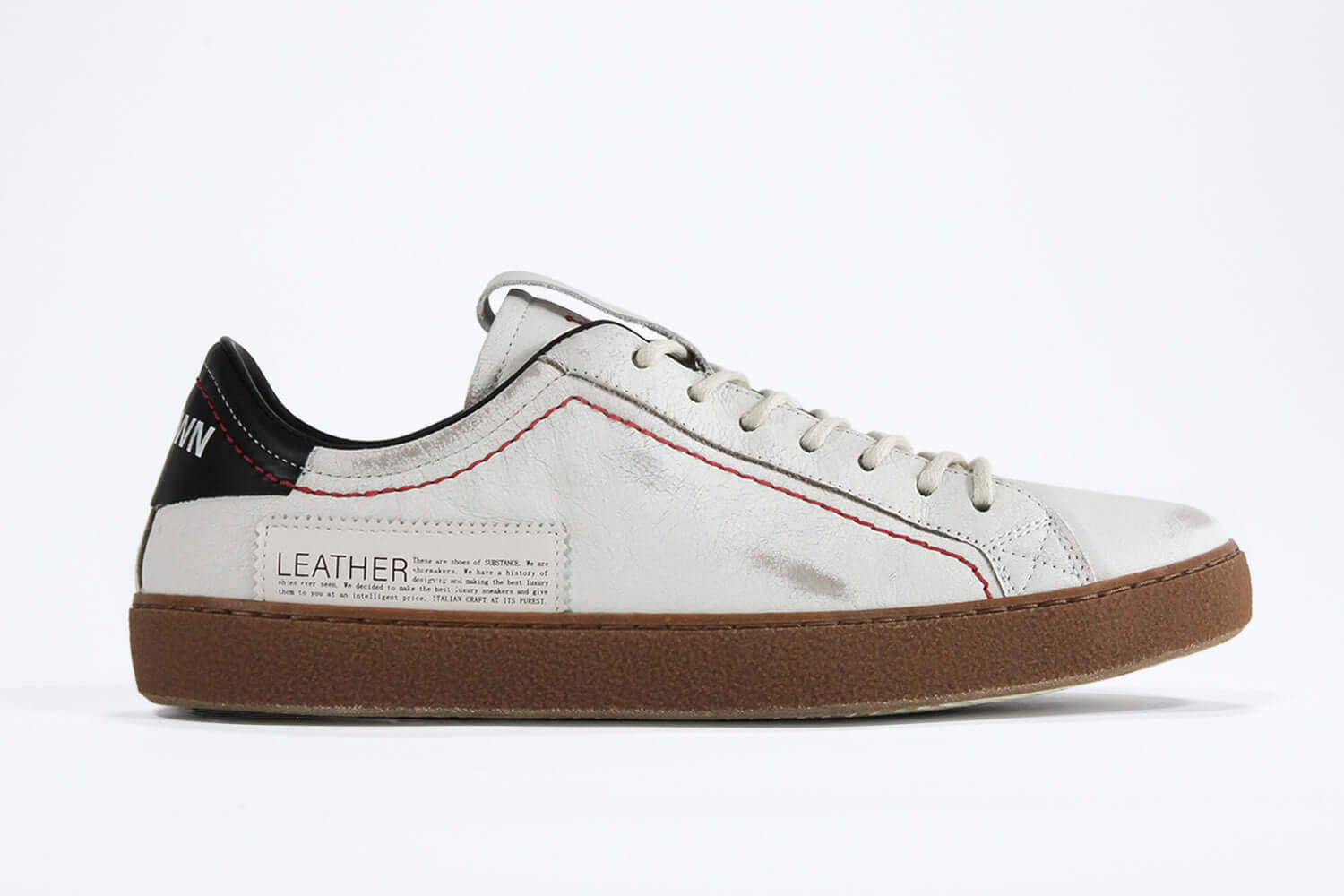Side profile of low top white sneaker with black accent. Distressed white leather upper with red stitching and dark rubber sole.
