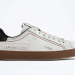 Side profile of low top white sneaker with black accent. Distressed white leather upper with red stitching and dark rubber sole.