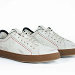 Three quarter front view of low top white sneaker with black accent. Distressed white leather upper with red stitching and dark rubber sole.