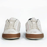 Front view of low top white sneaker with black accent. Distressed white leather upper with red stitching and dark rubber sole.