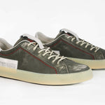 Three quarter front view of low top aged khaki sneaker with white accents. Perforated khaki leather upper with red stitching and pale natural rubber sole.