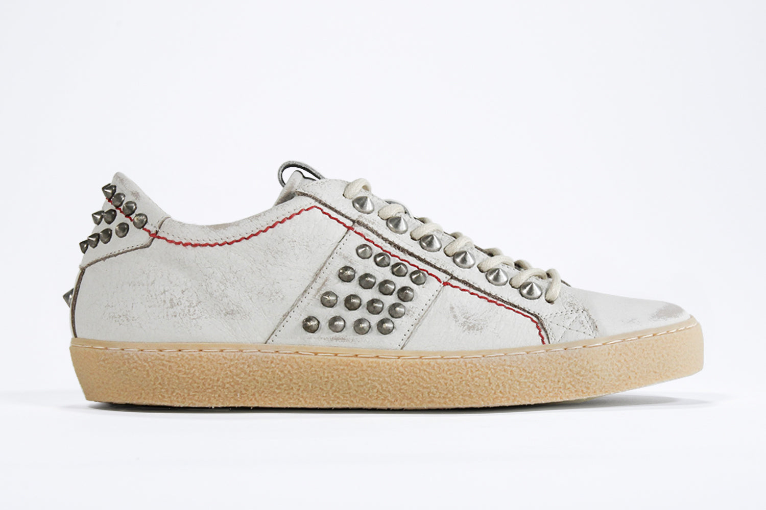 Side profile of low top white studded sneaker. Aged white leather upper with silver studs and natural rubber sole.