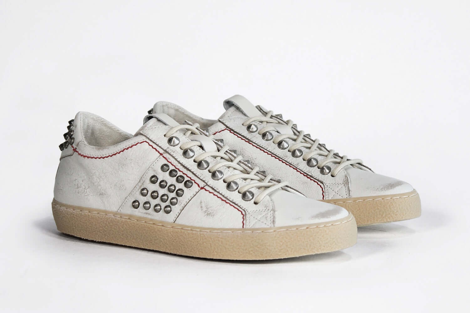 Three quarter front view of low top white studded sneaker. Aged white leather upper with silver studs and natural rubber sole.