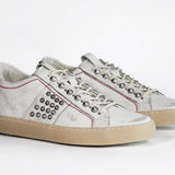 Three quarter front view of low top white studded sneaker. Aged white leather upper with silver studs and natural rubber sole.