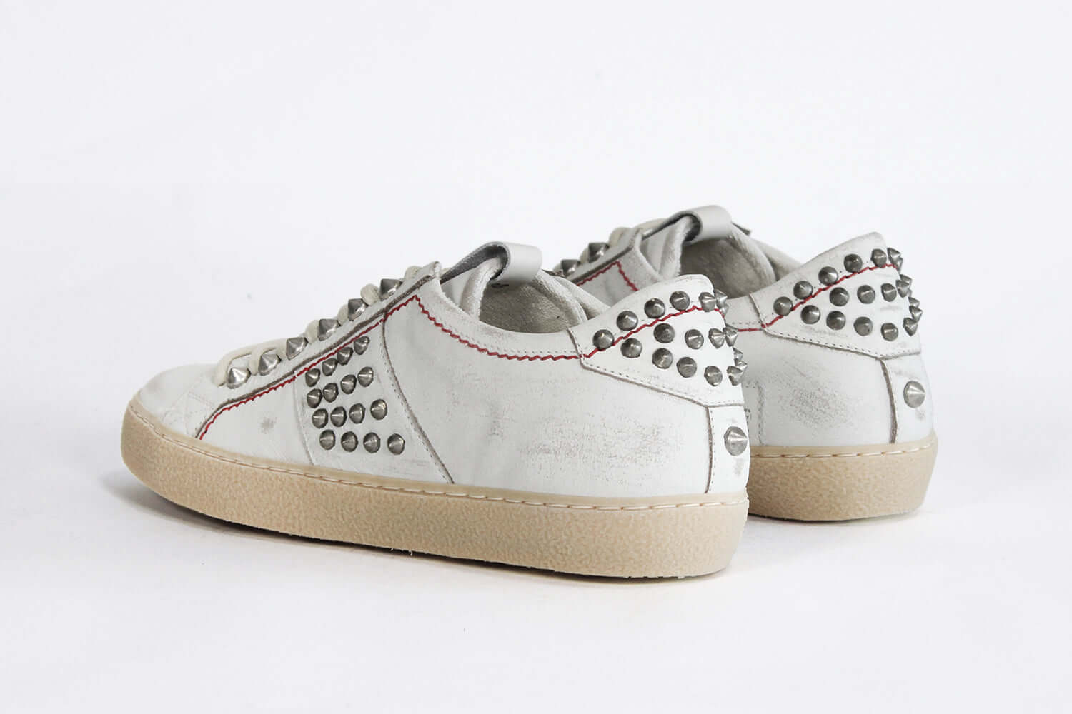 Back view of low top white studded sneaker. Aged white leather upper with silver studs and natural rubber sole.