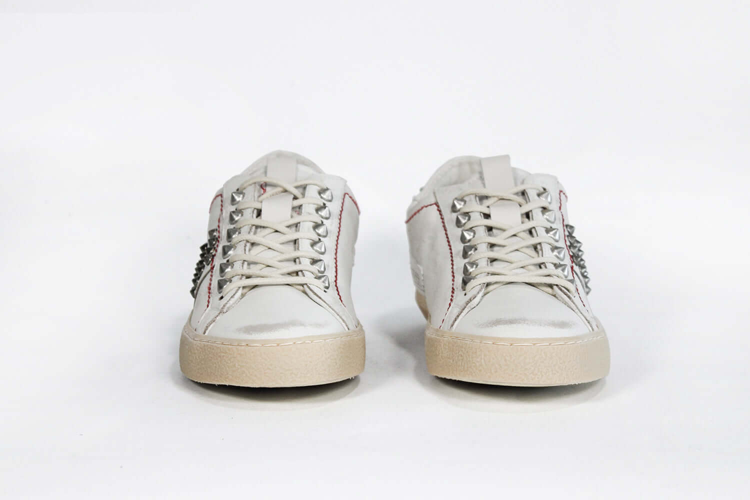 Front view of low top white studded sneaker. Aged white leather upper with silver studs and natural rubber sole.