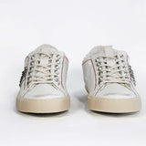 Front view of low top white studded sneaker. Aged white leather upper with silver studs and natural rubber sole.