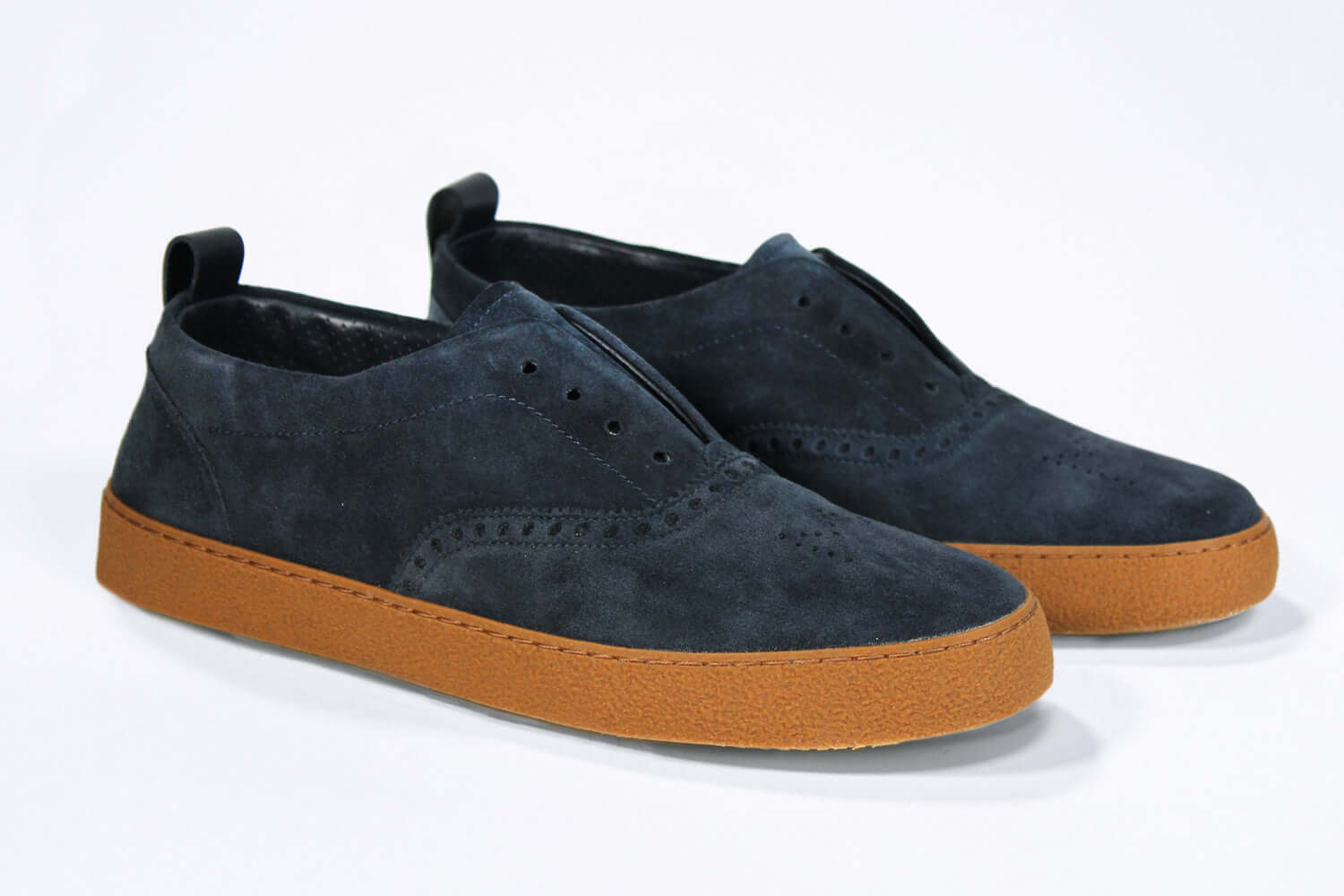 Three quarter front view of loafer style sneaker. Navy suede upper with perforated crown logo, elasticated tongue and a honey coloured recycled rubber sole.